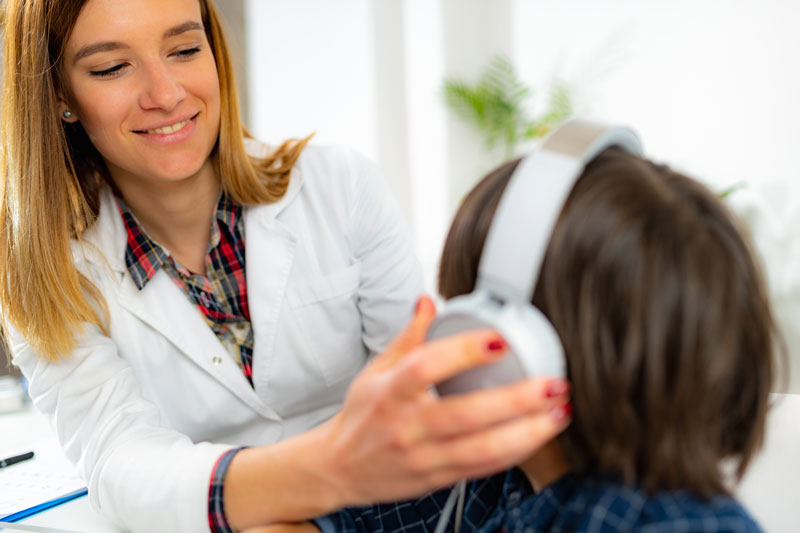 Female audiologist places headphones on young boy for hearing test