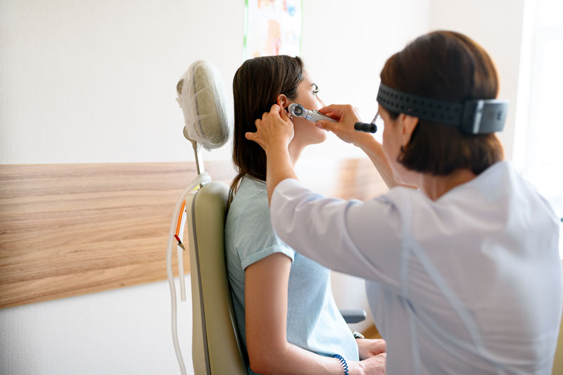 Female physician uses otoscope in ear of female patient