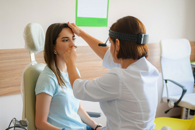 Female doctor uses scope to examine female patient’s nose