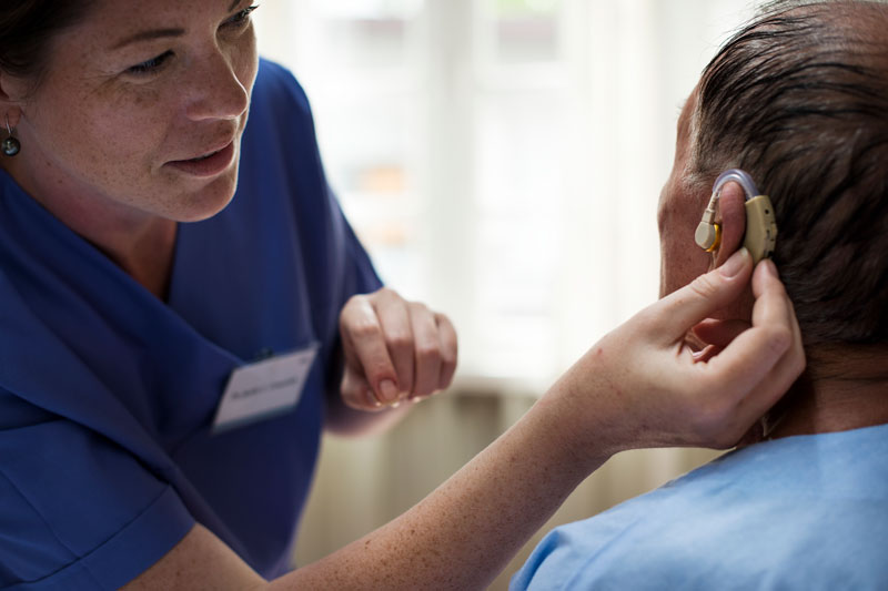 Woman wearing scrubs inserts a hearing aid into a male patient’s ear