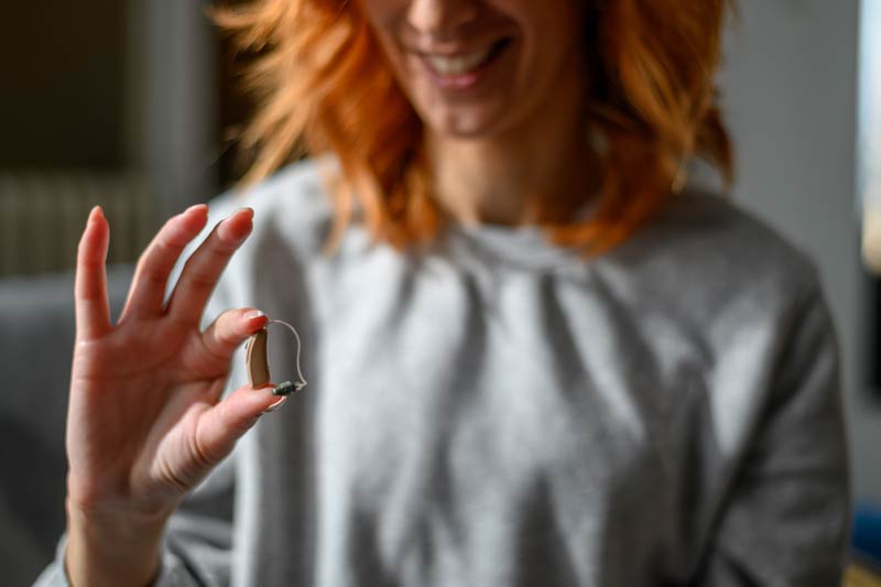 Woman holds a small hearing aid in her right hand