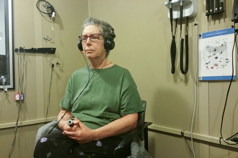 Elderly woman receives hearing test in a soundproof room given using headphones and a signaling device