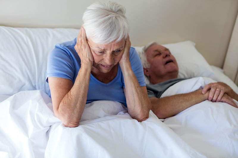 Senior woman getting disturbed with man snoring on bed
