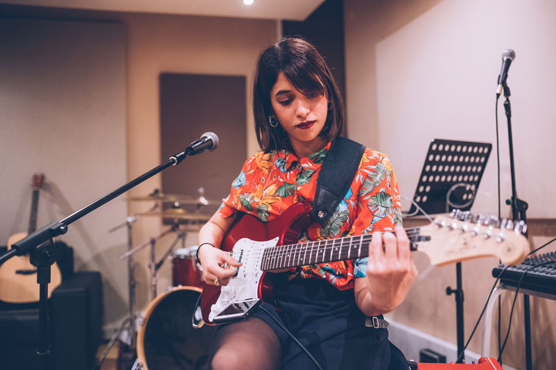 Female in music studio holding an electric guitar in front of a microphone