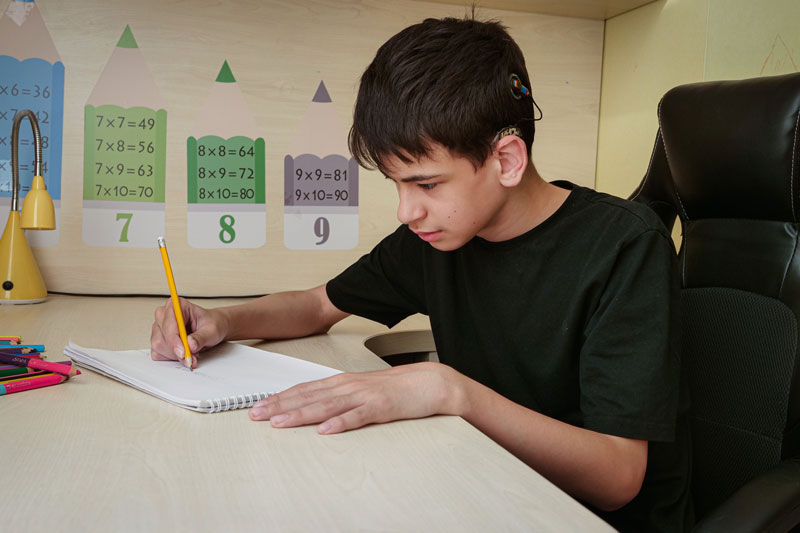 Teen boy sitting at desk with a cochlear implant