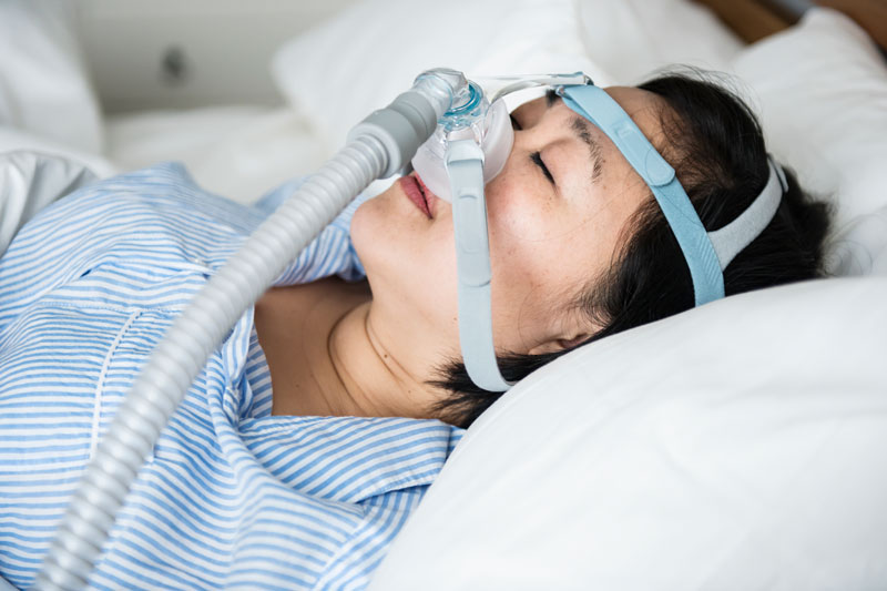 Woman laying in bed with hoses and mask for sleep apnea