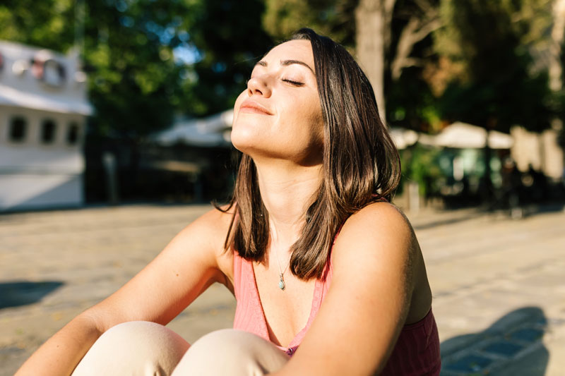 Woman sits outdoors with eyes closed breathing in