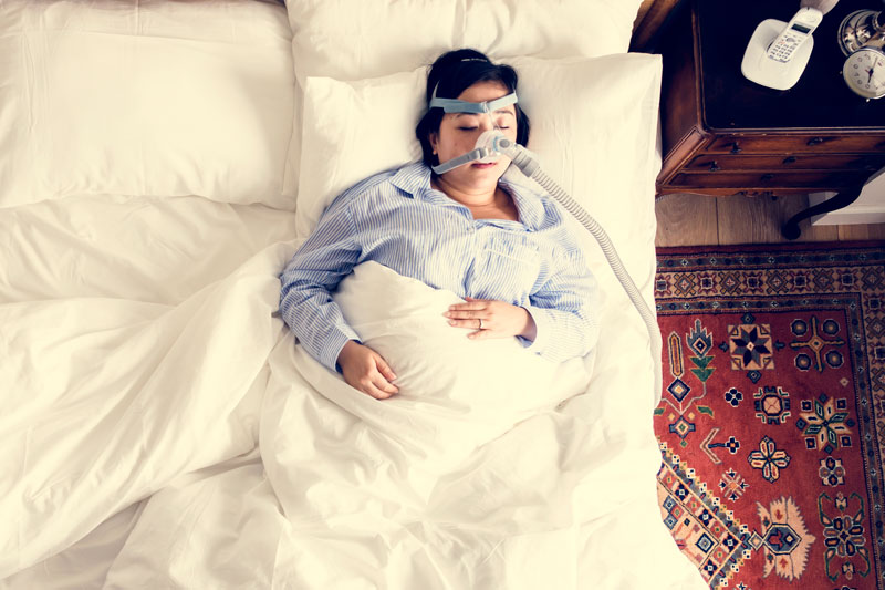 Woman sleeping in bed with CPAP mask and hose connected to her face