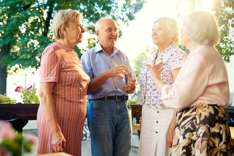 A group of four seniors standing together having a conversation outdoors