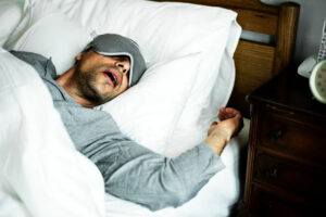 Man sleeps in bed with eye mask and mouth open