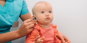 Photo of a baby in a pink dress receiving a hearing test from a clinician.