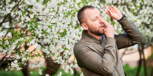 Man putting allergy eye drops in eyes while surrounded by flowers