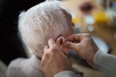 Close up of hearing aid being place into elderly man’s ear